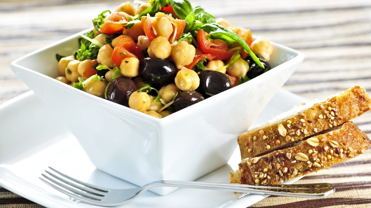 A salad bowl made with hardy chickpeas, salad greens, tomatoes, olives and extra virgin olive oil.