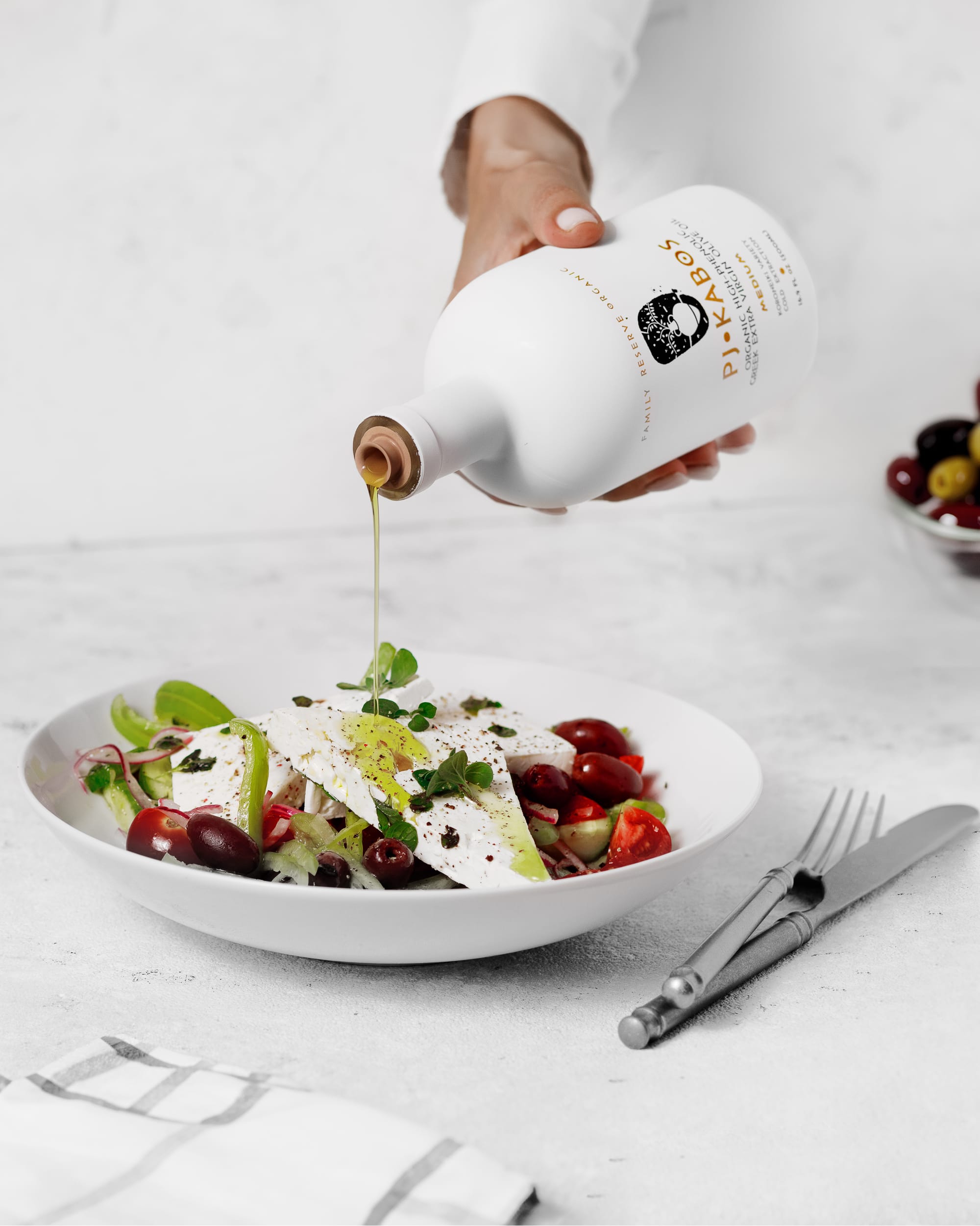 A bottle of Extra Virgin Olive Oil being poured over a Greek Village Salad.