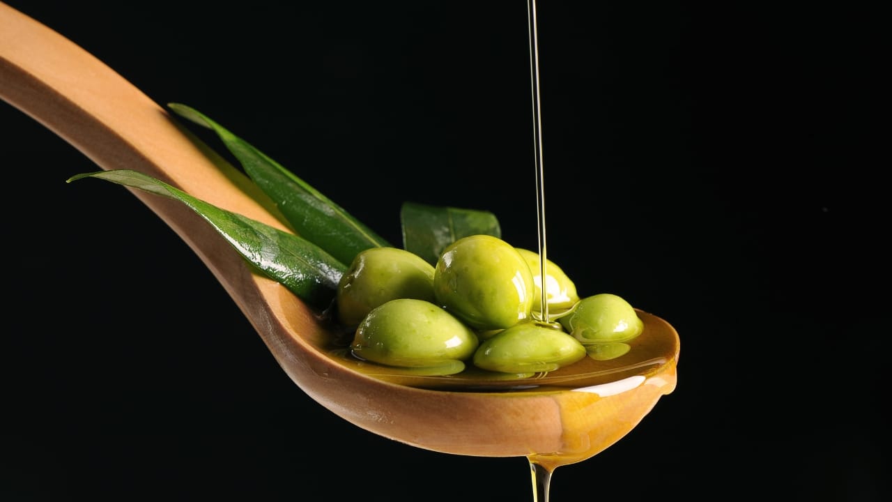 An artisanal wooden spoon cradles a bounty of olives, as the golden stream of precious extra virgin olive oil cascades over it in a picturesque dance.