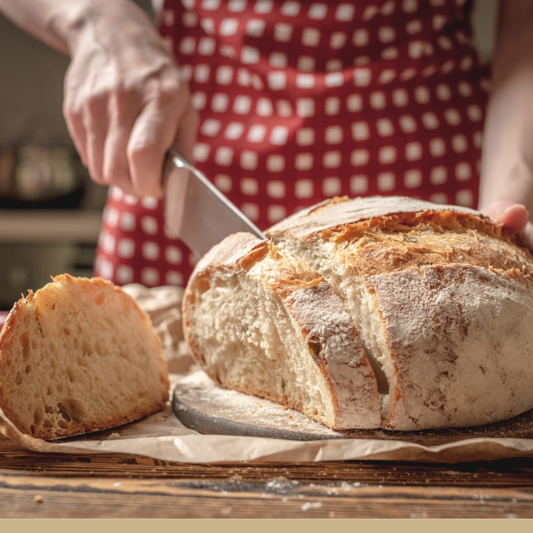 A woman slicing into a round loaf of freshly baked village bread.
