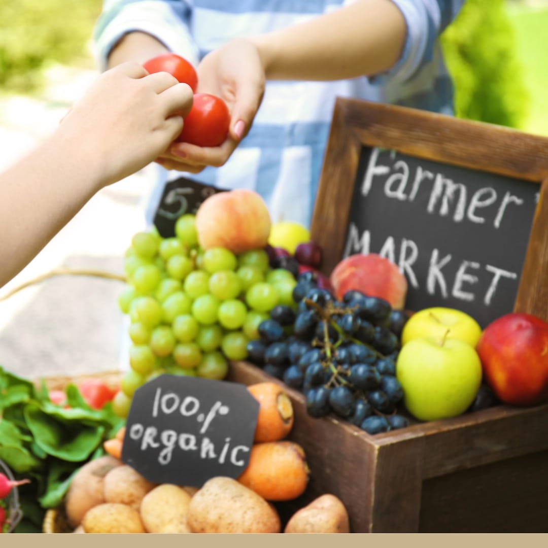 A farmer's market sign surrounded by fresh and organic carrots, potatoes, grapes, apples, etc.