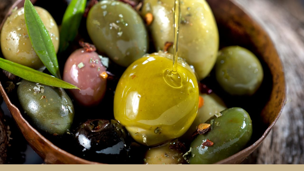 Olive oil is being dribbled over a bowl of olives.