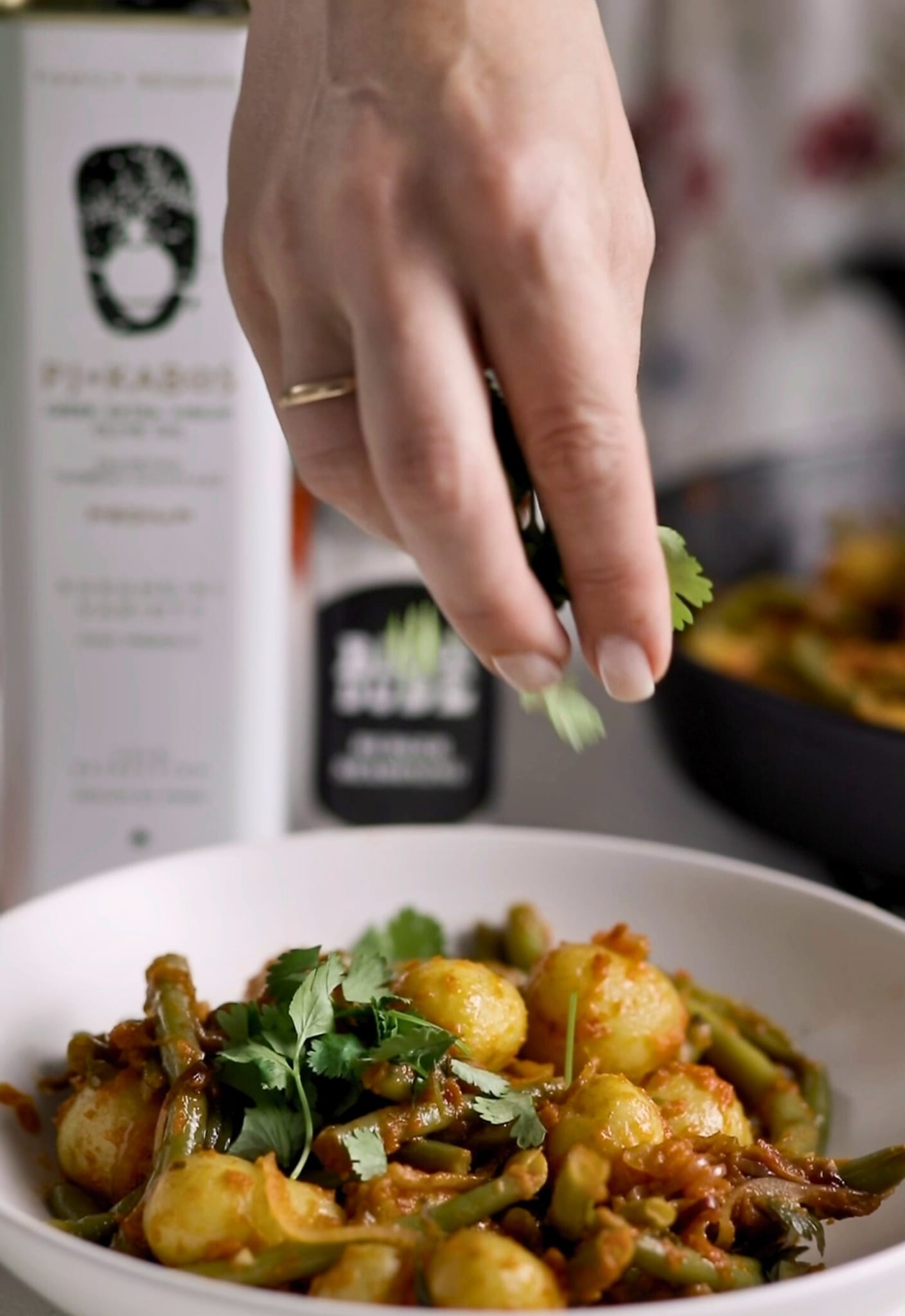 A woman is sprinkling fresh parsley leaves over a bowel of ready-to-serve braised green beans and potatoes.