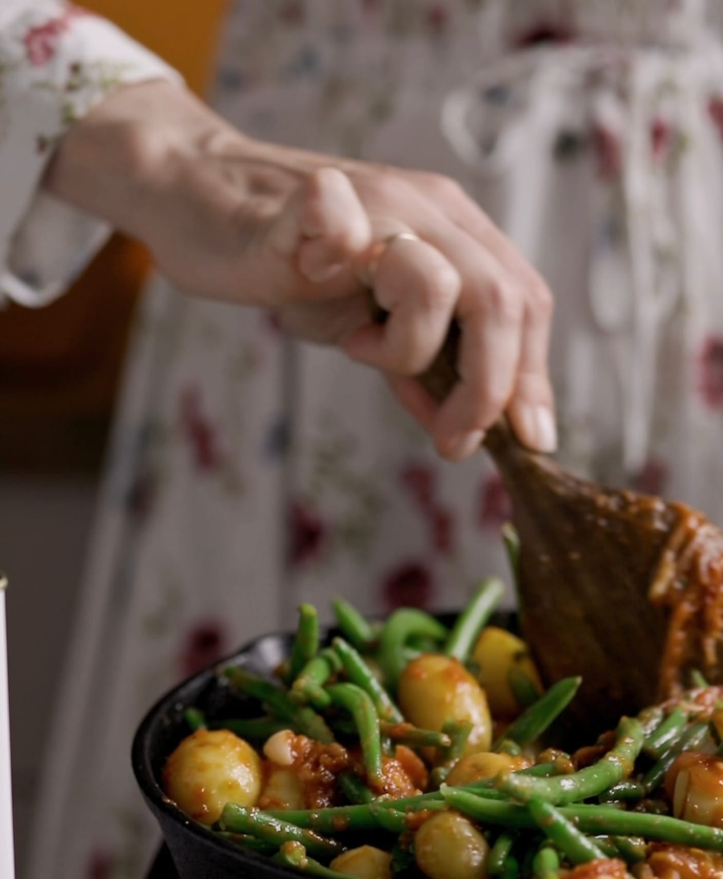 A woman is stirring a pan checking to see if the braised green beans she just cooked are done.